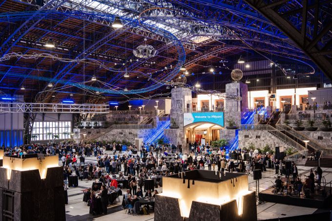 Large convention center floor with exhibitors, a large crowd, and interesting blue and purple grid of lights on the ceiling