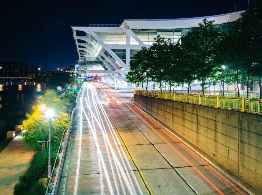 Red and white streaks on a road from time lapse photo with a dark night sky in the background and the curved roof of the Pennsylvania Convention Center as the image highlight